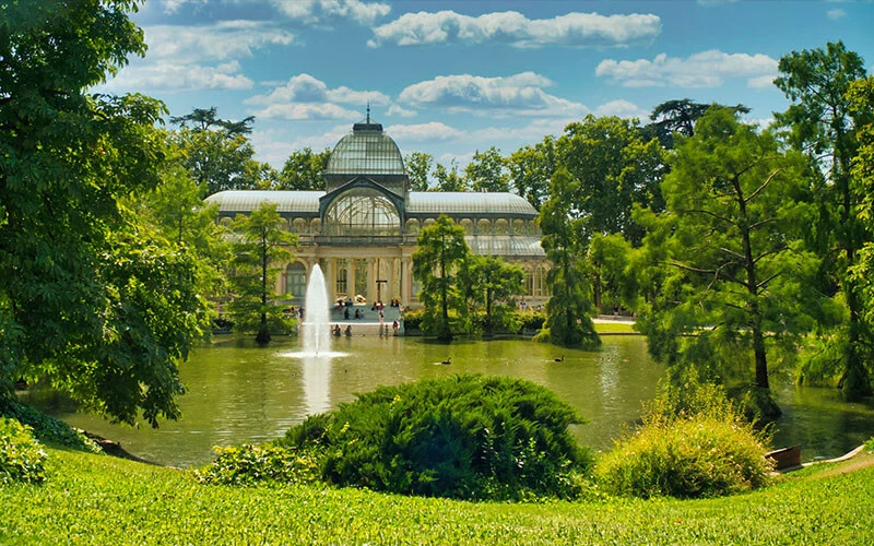Palacio de Cristal en el Parque del Retiro rodeado de naturaleza y un lago.