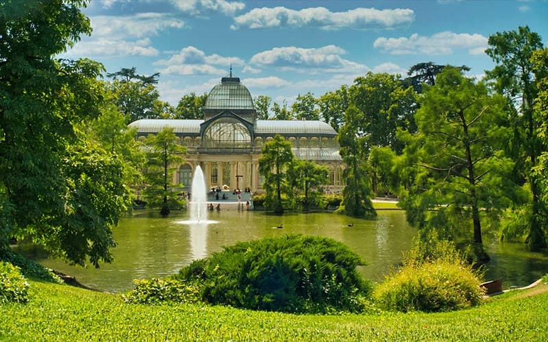 Palacio de Cristal en el Parque del Retiro rodeado de naturaleza y un lago.